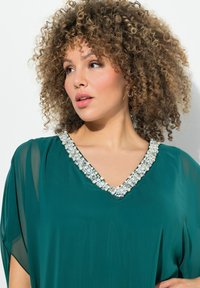 Aquafarbene Chiffon-Bluse mit V-Ausschnitt, verziert mit Perlen- und Kristallakzenten um den Kragen, mit locker sitzenden Ärmeln.