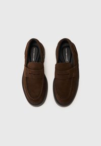 Mocassins en suède marron avec un bout arrondi, des coutures décoratives et une bride sur le cou-de-pied. Semelles intérieures noires confortables et semelles flexibles.