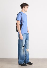 Jasnoniebieski t-shirt z krótkim rękawem zestawiony z szerokimi, przetartymi niebieskimi dżinsami. Czarna torba na ramię zarzucona na jeden bok. Czarne buty dopełniają całość.