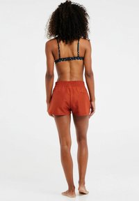 Shorts de color óxido con cintura elástica y un bolsillo trasero, combinados con un sujetador tipo bralette de lunares negros. Tela suave, diseño casual.