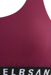 Top sportivo color bordeaux con un tessuto morbido, scollatura rotonda e una banda nera a contrasto con testo bianco. La texture è morbida ed elastica.