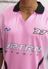 Roosa spordijERRIDE Jersey musta krae, millel on täppide muster, suur "URTRN" logo ja "97" graafika. Valmistatud sujuvast kangast.