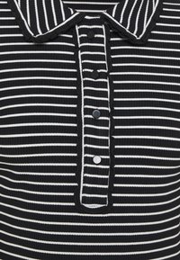 Camisa polo a rayas en blanco y negro con un cuello ondulado, cinco botones negros y textura acanalada en la tela.