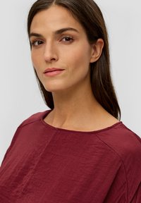 Burgunderfarbige Bluse mit weitem Ausschnitt und weichem, strukturiertem Stoff. Verfügt über eine lockere Passform und genähte Nahtdetails an den Schultern.
