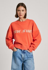 Felpa color corallo con scollo rotondo e spalle abbattute. Presenta il logo "PEPE.JEANS" in beige a contrasto sul petto.