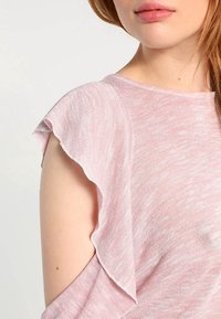 Haut rose et léger avec des manches à volants et une texture légèrement transparente. Le tissu présente une apparence douce chinée avec des variations subtiles.