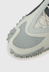 Světlé šedé atletické boty s texturovaným síťovaným svrškem, koženými překryvy a odolnou gumovou podrážkou s vystoupajícími trakčními výstupky.