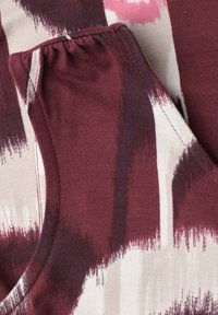 Gros plan sur un tissu avec un motif abstrait de coups de pinceau bordeaux, rose et blanc et un détail élastique froncé sur une manche de vêtement.