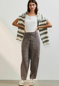 Losse grijze cargobroek met voorzakken, gecombineerd met een witte top en een gestreepte gebreide cardigan over de schouders.