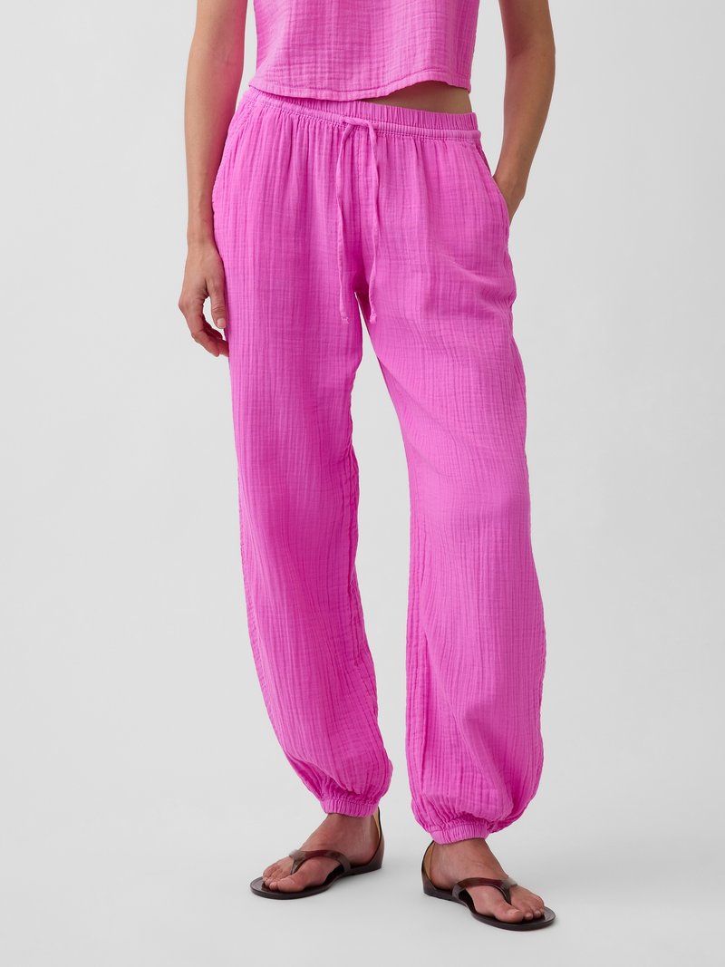 Femme portant un pantalon ample rose texturé avec poignets élastiques et taille à cordon, associé à des sandales marron sur un fond uni.
