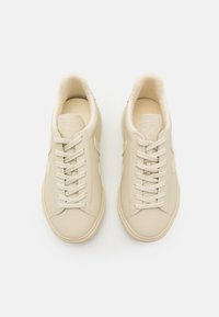 Pár béžových kožených tenisek s tkaničkami a fleecovou podšívkou, pohled zhora na bílém pozadí.