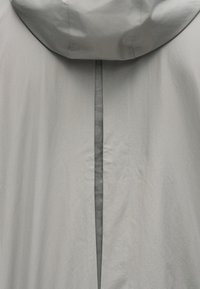 Lichtgrijs gewatteerd jack met capuchon en een verticale achterventilatie die een donkere binnenlaag met een subtiel tekstpatroon onthult.