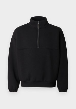 Juoda džemperis iš minkštos medžiagos, su pusiau užtrauktuku prie apykaklės, ilgomis rankovėmis ir aptemptais rankogaliais bei apačia, užtikrinančiais laisvą prigludimą.