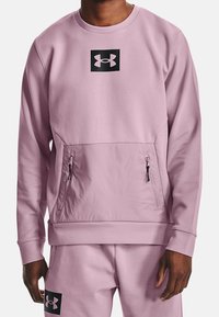 Felpa rosa chiaro con logo Under Armour nero sul petto, dotata di tasca frontale con due cerniere e polsini a costine.