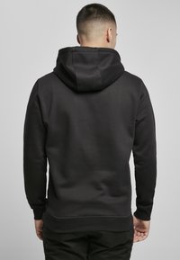 Černá mikina s kapucí, měkkou texturou, mírným strečem a žebrovanými manžetami. Obsahuje klokankovou kapsu a jednoduchý design.