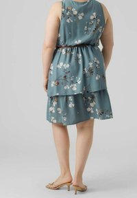 Sømløs teal kjole med blomsterprint, tieret design og elastisk talje. Har let stof og flade sandaler med små hæle.