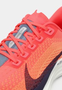 Φωτεινό κοραλί Nike Pegasus αθλητικό παπούτσι με κοραλί κορδόνια, μπλε γλώσσα και μαύρο λογότυπο Nike στο υφασμάτινο άνω μέρος.