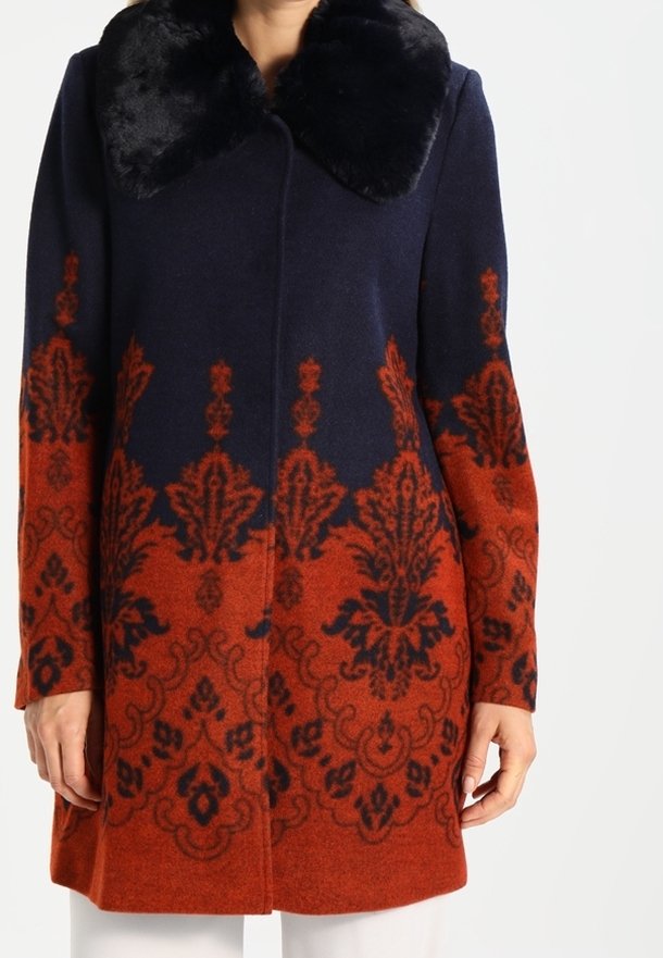 Uldfrakke med en navy øverste og en orange nederste del med indviklede blomster mønstre. Sorte faux fur krave og lige snit design.