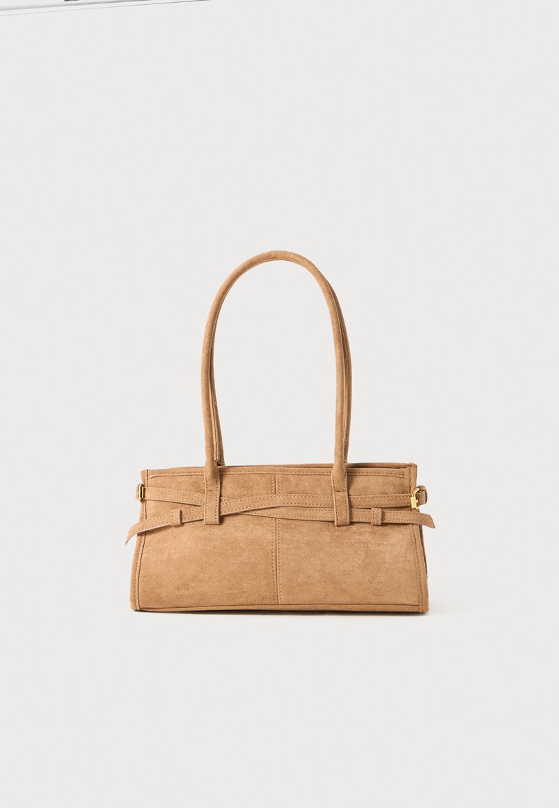 Sac en daim beige avec deux longues poignées, de forme rectangulaire et avec des coutures décoratives. Dispose d'une bandoulière et de subtils accents en métal doré.