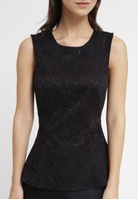 Top senza maniche nero caratterizzato da un motivo in pizzo floreale testurizzato e una silhouette aderente con un dettaglio a peplum in vita. Finitura liscia.