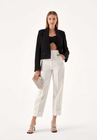 Čierny skrátený blazer, čierny bandeau top, biele nohavice s vysokým pásom a manžetami, strieborné sandále na blokovom podpätku a strieborná kabelka.