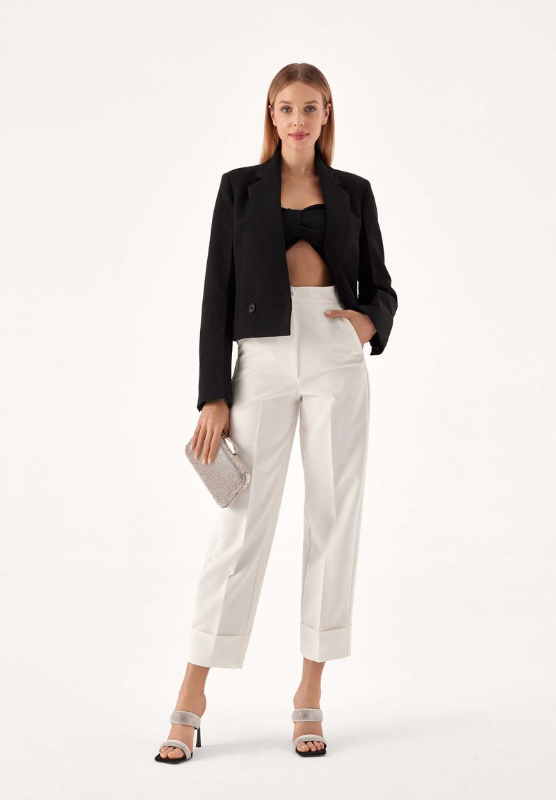 Čierny skrátený blazer, čierny bandeau top, biele nohavice s vysokým pásom a manžetami, strieborné sandále na blokovom podpätku a strieborná kabelka.