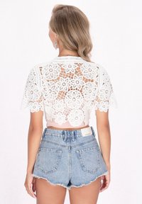 Top corto in pizzo bianco con motivi floreali e maniche corte, abbinato a pantaloni da denim a vita alta di colore blu chiaro con orli sfrangiati.