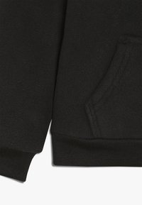 Svart fleece-tyg med en sidoficka, som har en texturerad ribbad mudd. Materialet är mjukt, med en slät yta och rena sömmar.