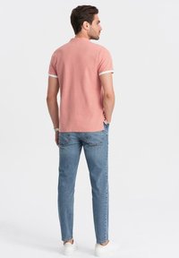 Polo shirt rosa con bordi bianchi, abbinato a jeans azzurri chiari. La camicia presenta un colletto classico e un design a taglio dritto.