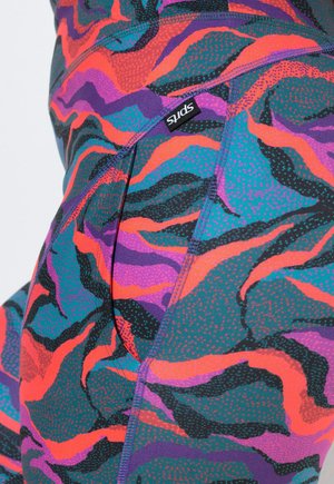 Obcisłe legginsy z żywymi falistymi wzorami w kolorach morskim, fioletowym, pomarańczowym, czarnym i różowym, z małą czarną metką z białym napisem "SPIRITS".