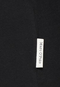 Tela negra con una textura suave, con una pequeña etiqueta blanca que dice "Marc O'Polo". Etiqueta cosida en la costura lateral.