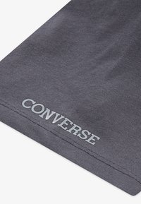 Grå bomullstoff med en teksturert overflate. Har en hvit "CONVERSE" logo nederst. Enkel, uornamentert design.