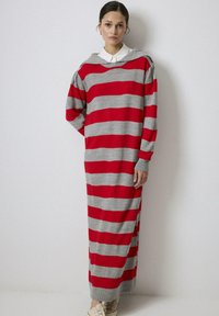 Rochie de tip pulover supradimensionată cu dungi roșii și gri, cu glugă, manșete și tiv cordonate, având o croială liberă și o textură moale de tricot.