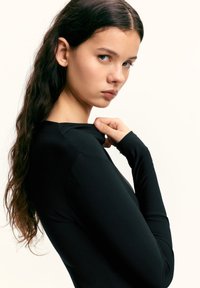 Fekete hosszú ujjú felső sima, rugalmas anyagból. A kialakítás kerek nyakkivágással és testhez simuló sziluettel rendelkezik.