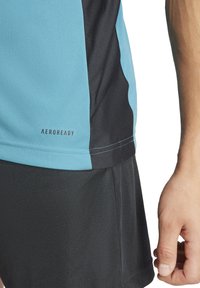 Top sportivo in blu chiaro e nero, realizzato in tessuto traspirante con etichetta AEROREADY, caratterizzato da blocchi di colore a contrasto e superficie liscia.
