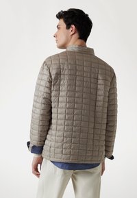 Pelēka quilted jaka ar augstu apkakli, kas iezīmēta ar izšūtiem kvadrātiem un gludu tekstūru. Jaka ir ar ruļļu piedurknēm un brīvu piegriezumu.