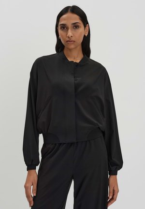 Zwarte cropped jas met knoopsluiting, zijzakken en oversized mouwen. Gladde textuur en minimalistisch ontwerp.