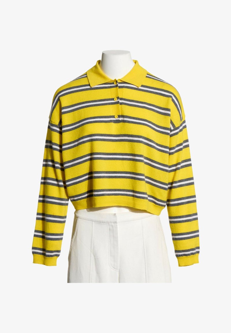 Pull polo jaune cropped à manches longues avec des rayures horizontales grises et blanches, associé à un pantalon blanc taille haute sur un mannequin.