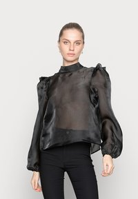 Blusa preta translúcida com ombros franzidos, gola alta e mangas longas bufantes. Textura suave e corte ligeiramente solto.
