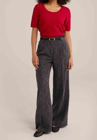 Pull rouge à manches courtes texturé associé à un pantalon large anthracite taille haute, rehaussé d'une ceinture noire et de chaussures en mesh noires.