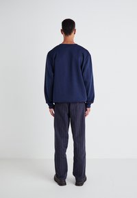 Navy sweatshirt with a relaxed fit, round neckline, paired with pinstriped gray pants. Smooth texture and subtle, minimalist design.
