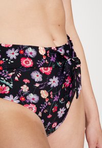 Parte de baixo de bikini de cintura alta com um fundo preto, apresentando padrões florais vibrantes em várias cores. Inclui um detalhe de laço lateral.
