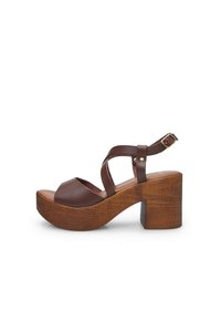 Brown leather heeled sandals with a platform, featuring crisscross straps and a sturdy wooden block heel. Smooth texture with metal accents.