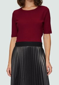 Top de manga corta de canalé burdeos combinado con una falda negra plisada que cuenta con una cintura elástica. Textura suave y diseño ajustado.