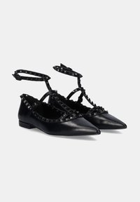 Bailarinas de cuero negro con puntas afiladas, decoradas con tachuelas en forma de pirámide a lo largo de las correas y una doble correa en el tobillo para un ajuste seguro.