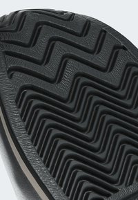 Black rubber shoe sole with a zigzag tread pattern, featuring textured grooves and a smooth border. Durable and flexible design.
