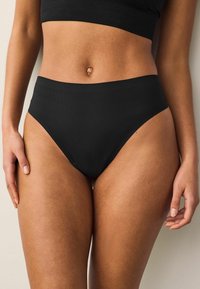 Culottes noires taille haute avec une texture douce et nervurée, présentant un design minimaliste et des bords sans couture pour le confort et l'ajustement.