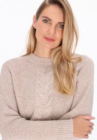 Pullover tricotat de culoare bej deschis, având un design cu model de cablu în față, guler și manșete cu nervuri. Textură moale, cu o croială confortabilă.