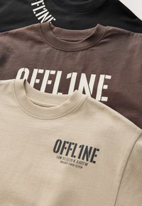 Drie sweaters in zwart, bruin en beige. Elk heeft de tekst "OFFLINE" in contrasterende kleuren. Geribbelde ronde hals en katoenmateriaal.