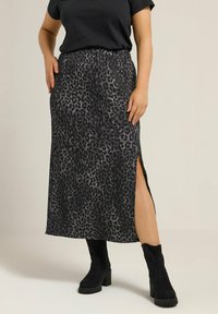 Maxi-jurk met luipaardprint, gemaakt van zachte stof met een zijsplit, gecombineerd met zwarte kniehoge laarzen. Beschikt over een elastische tailleband.